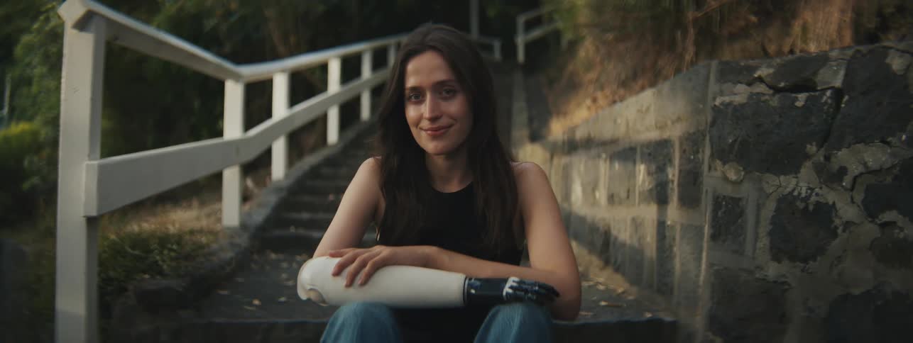 A woman is sitting on a staircase and is smiling and she has a prosthetic arm