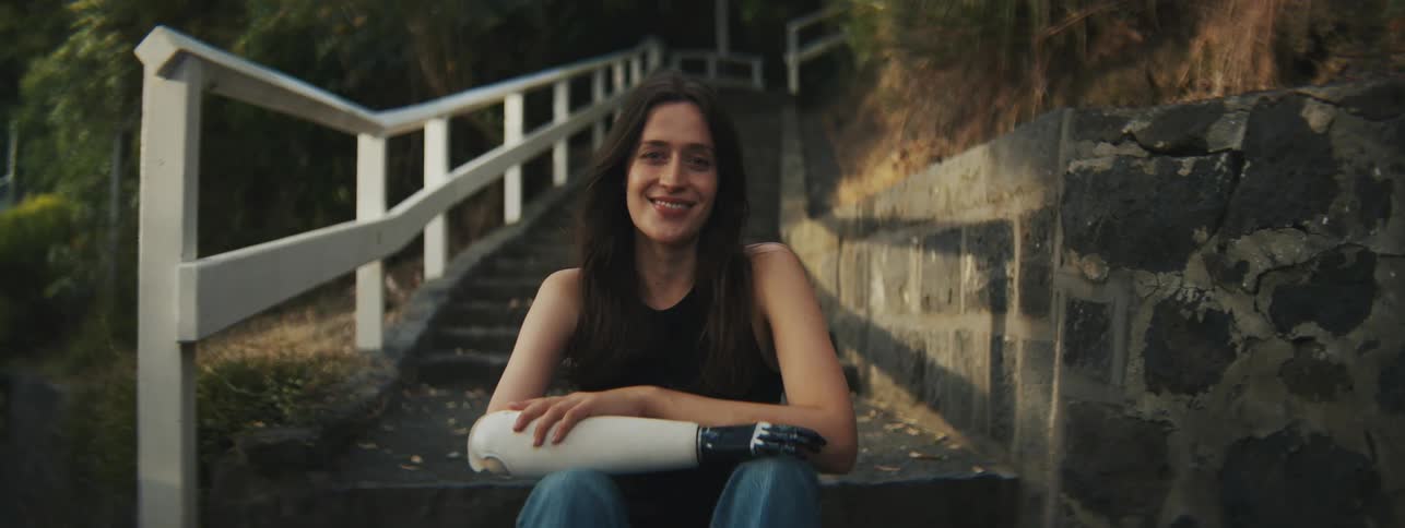 A woman with a prosthetic arm sits near outdoor stairs