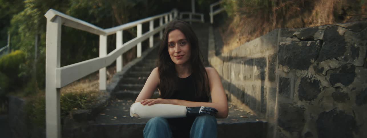 A young woman sitting on a step of a stone staircase and using a prosthetic in place of her arm