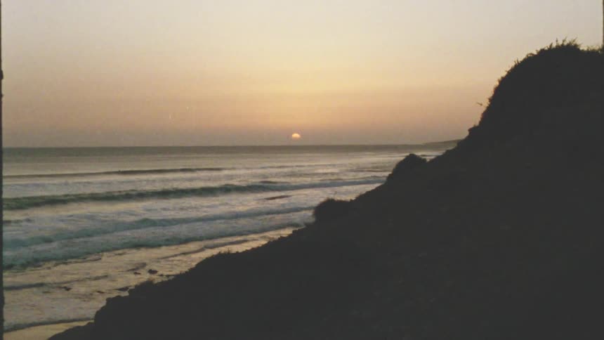 The waves crash against the shore at sunset