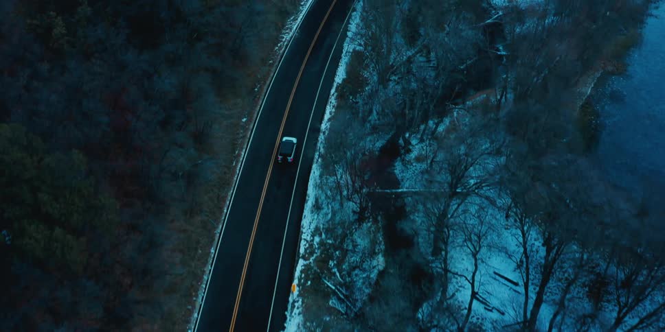 Car drives down an empty highway that divides a snowy forest