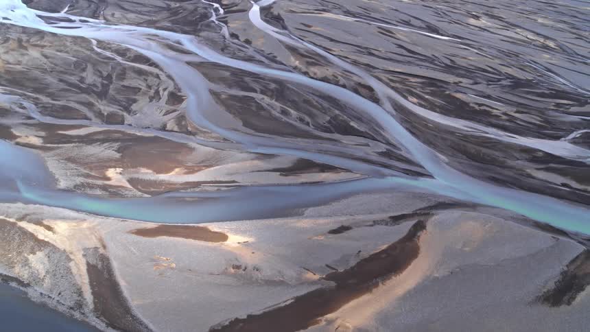 Aerial view of a braided river weaving through a melting glacial terrain at sunrise