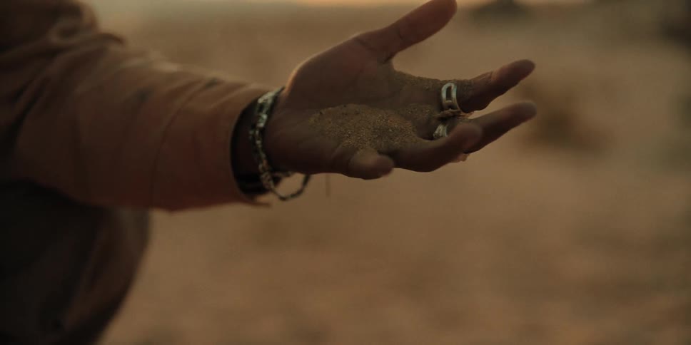 A native american lets sand drain through his fingers in a desert