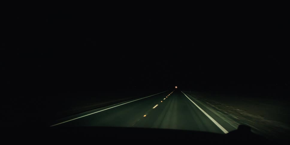 View of the inner windshield of a vehicle moving along a paved road in a deserted location at night