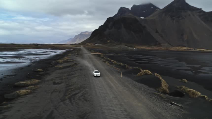 The car drives on the dirt road by the mountain