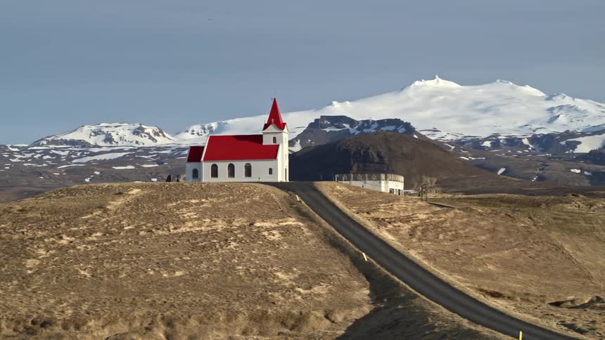 A church sits in the middle of a grassy plain near a mountain range