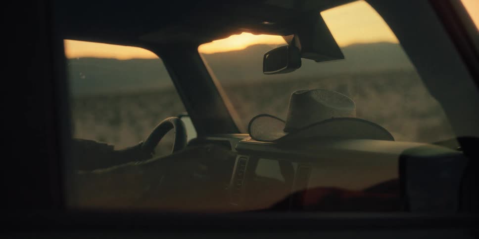 Person inside the car taking off their hat and placing it next to the windshield while in a natural environment