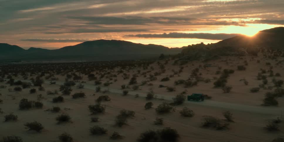 Aerial panorama of a jeep traveling on a street in a deserted location with sunrise on the horizon