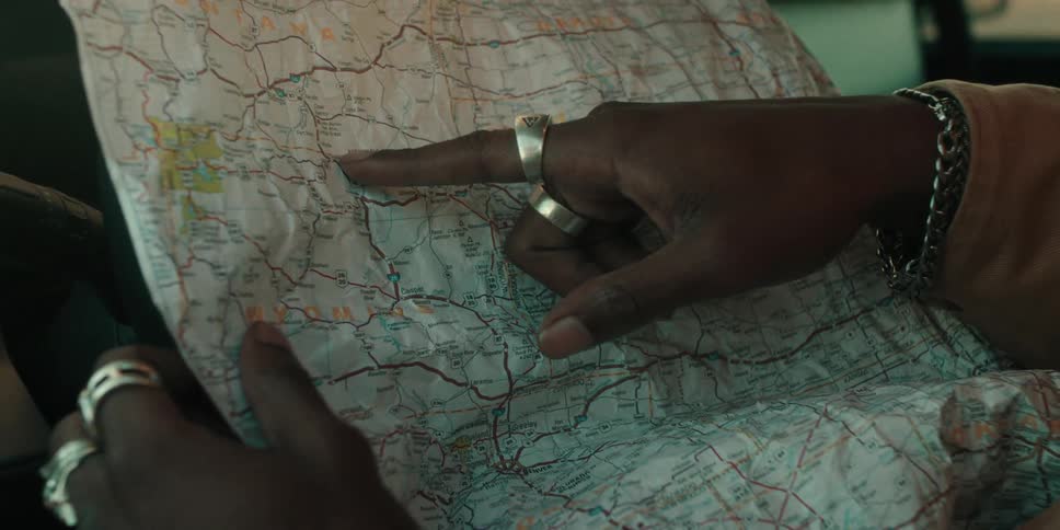 A black adult points a finger along a road map while sitting in a vehicle