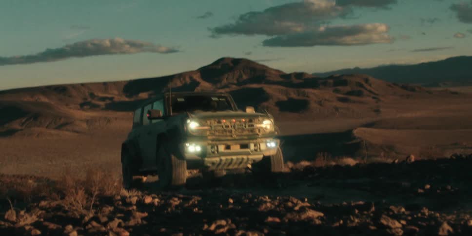 Jeep climbs a soft dirt road up a hill with mountains behind it