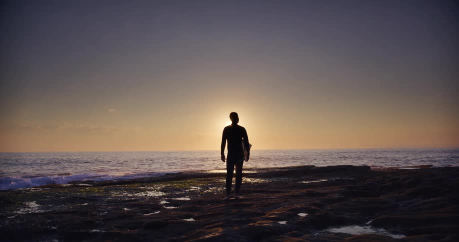 Silhouette of a man on a rock by the sea with sunrise on the horizon