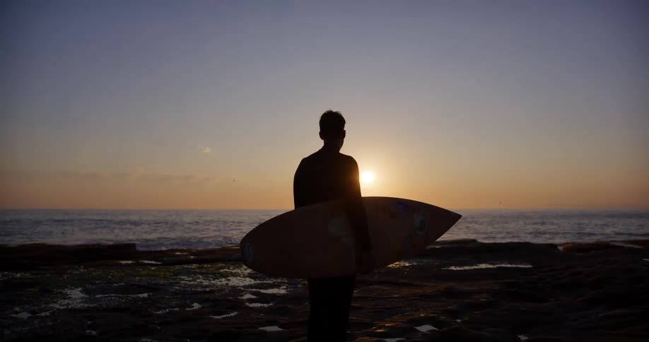 A man stands on the beach holding his surfboard