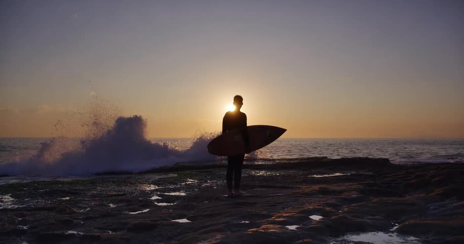 A surfer stands on a beach watching the waves break