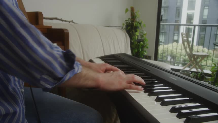 Man indoors setting up his laptop and then playing the electronic piano