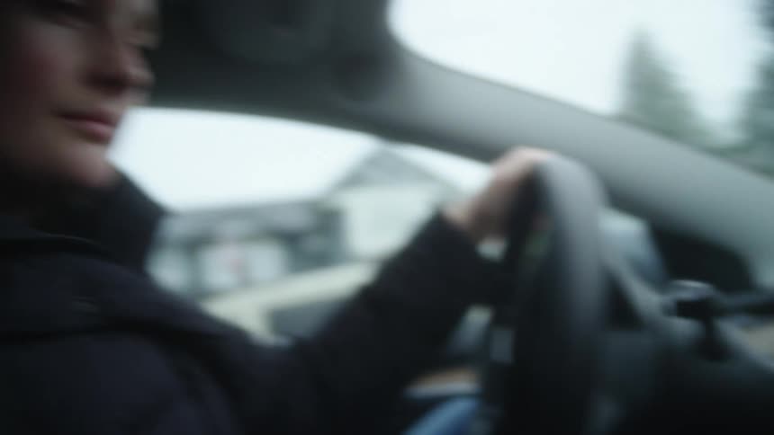 Woman moves a map around with her fingers on car gps touchscreen with one while holding the steering wheel with the other hand and looking thoughtfully at the screen on a cloudy winter day
