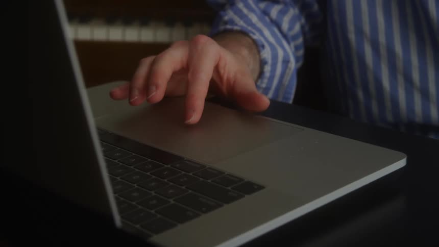 Man in blue pin stripe shirt moving fingers on a laptop touchpad while bouncing around unsteadily