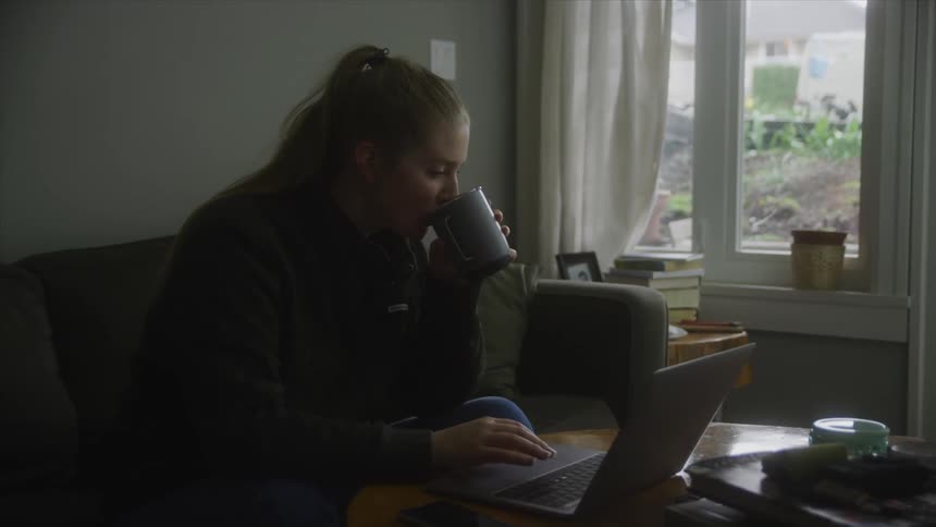 Woman sitting on couch and typing on laptop near window