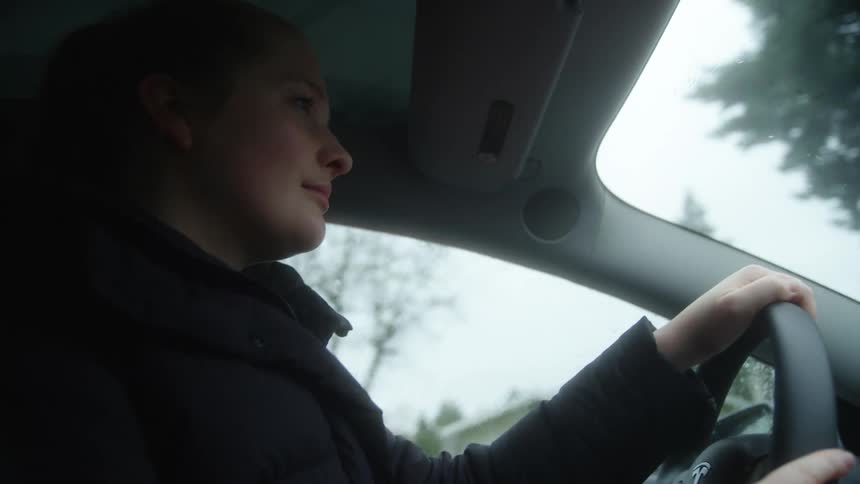 A slightly smiling woman drives her car through a suburban area