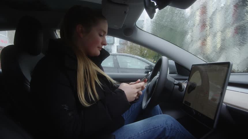 A woman gets into her parked car and texts on a cellphone