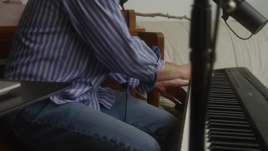 Male musician using headphones and a laptop plays keyboards