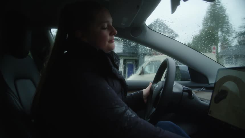 Woman is sitting in her car while its raining outdoors