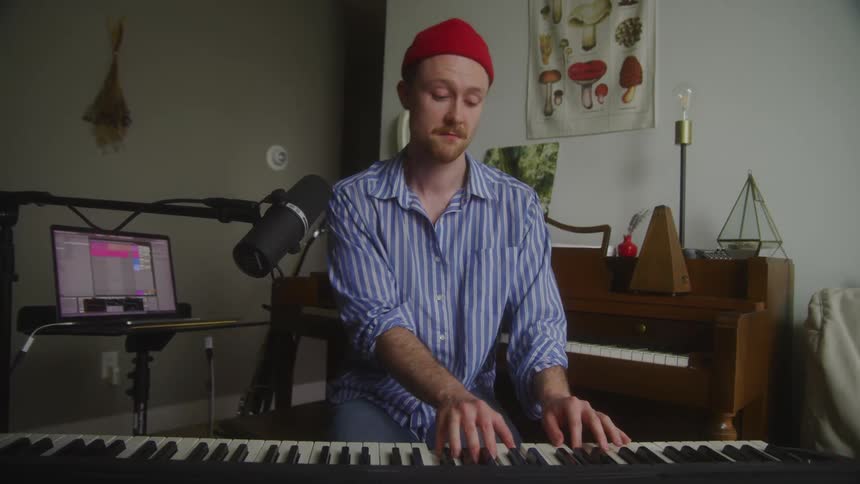 A musician plays a keyboard and then checks a laptop
