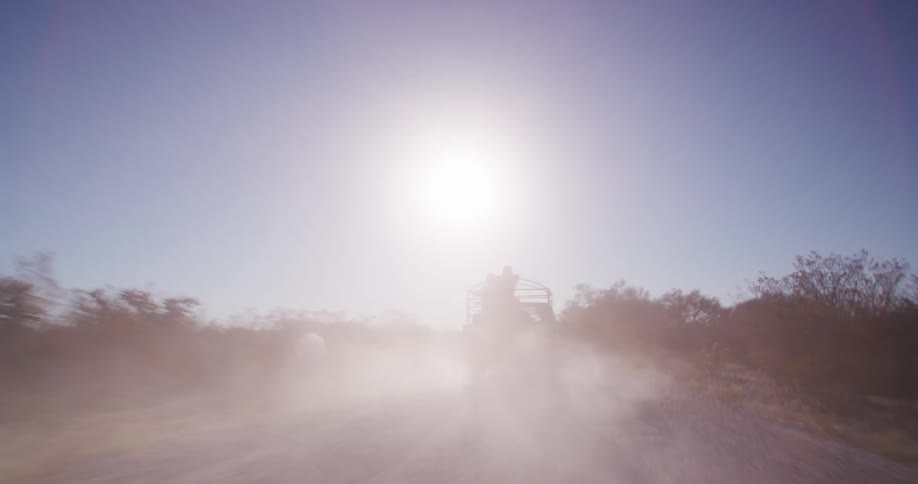 Vehicle drives down a dirt road toward the sun