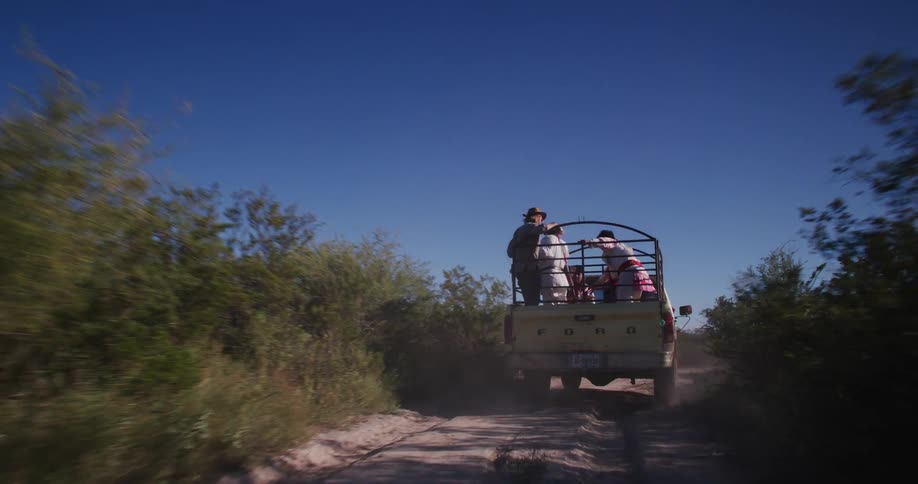 People are riding on the back of a truck on sandy terrain