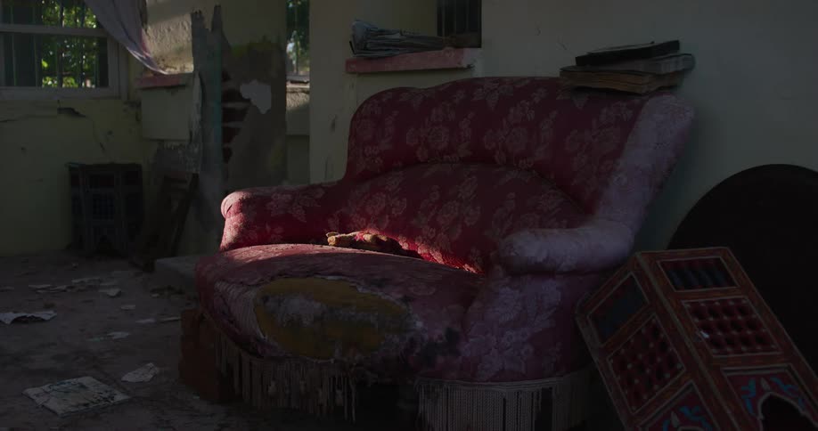Interior architecture of a room in a destroyed house with a precarious sofa and sunlight reflection