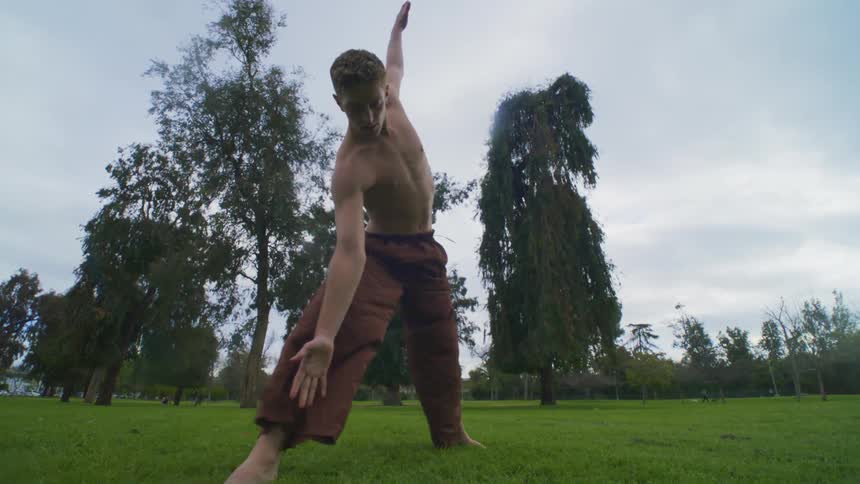 A muscular shirtless man stretching on a park