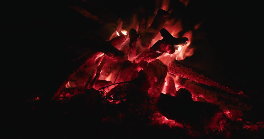 Logs in a bonfire are lit with flames at night