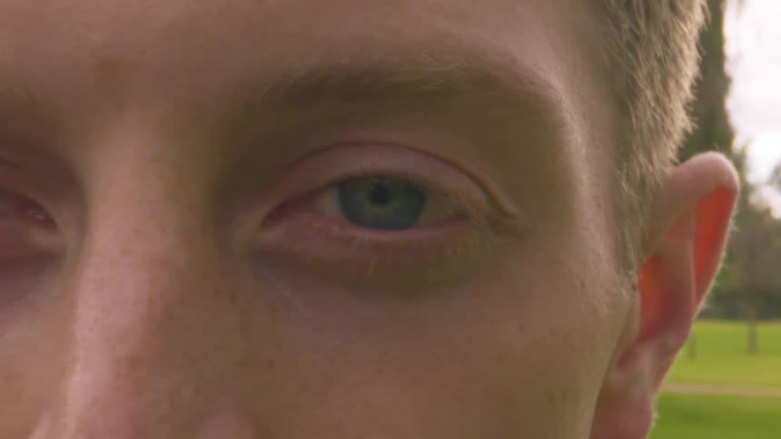A young man stands behind a branch blinking his eyes
