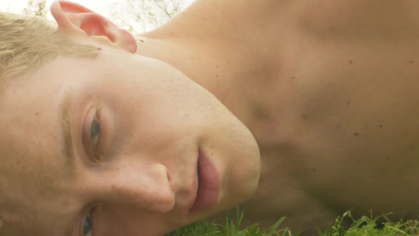 A white man lying on the ground makes a gesture with his hand