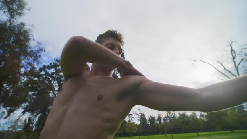 Shirtless man dancing and gesturing with his arms in a natural park