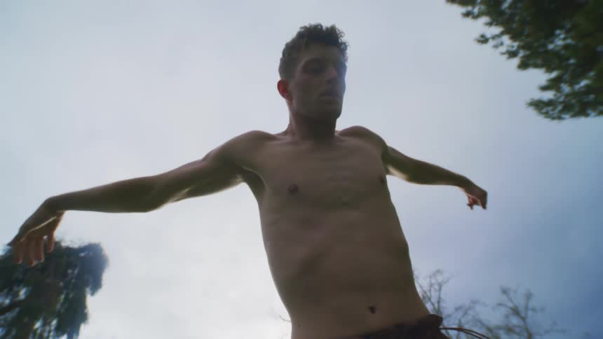 Shirtless man stretching his arms while standing in a garden park