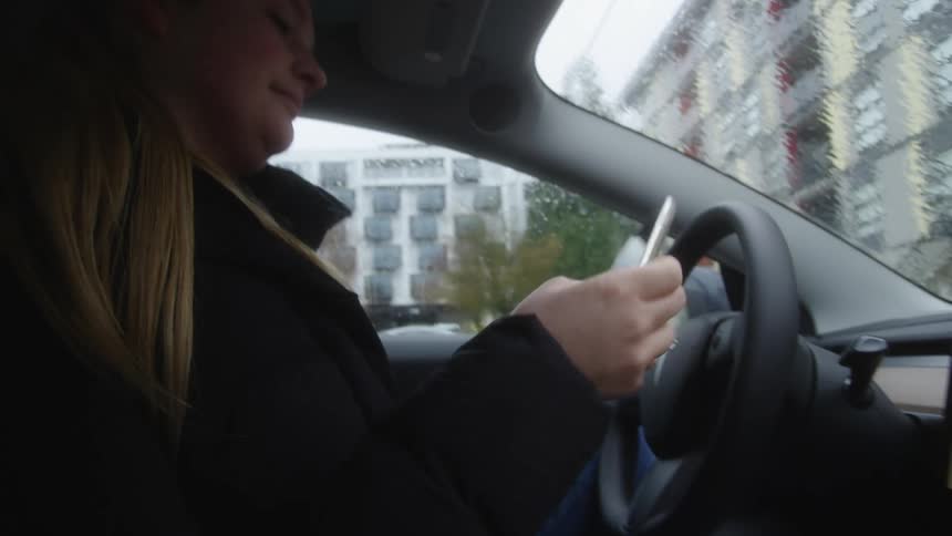 Young woman getting into her tesla and then using her cell phone