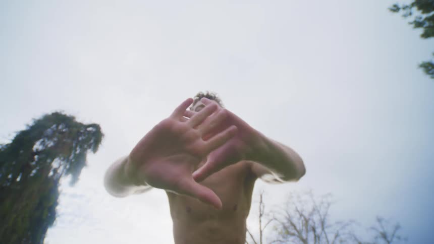 Shirtless man in a cloudy outdoor environment dancing in a scenic manner