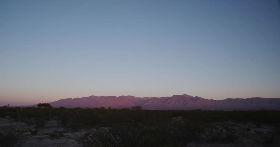 Landscape view of a desert with a large mountain range in the distance at dusk