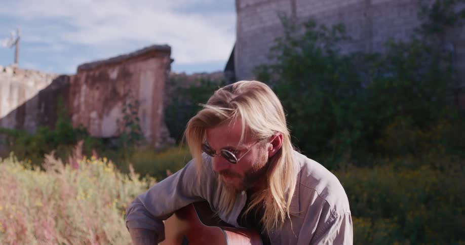 Man with sunglasses outdoors playing guitar