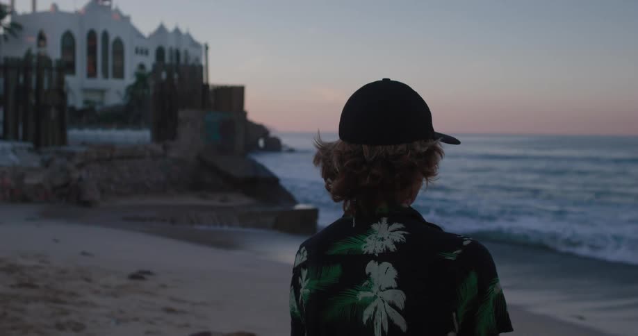 Person in a hawaiian shirt watches the waves lap the beach near a white castle