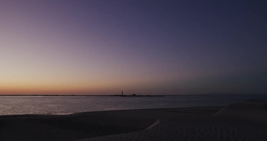 A beach at sunset with a lighthouse in the distance
