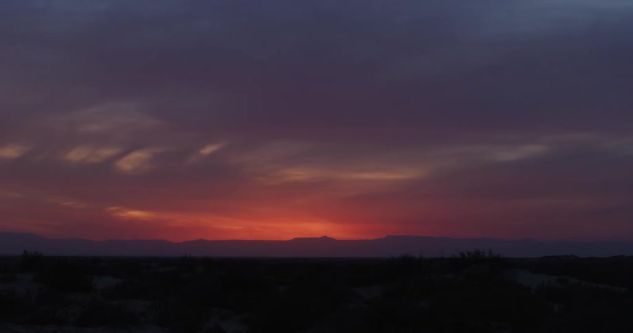 A sunset over a desert landscape with mountains in the distance