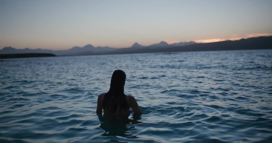 Silhouette of a woman entering a lake in the mountains at dusk