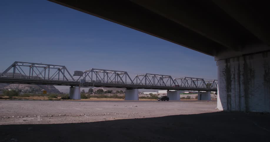 Motorcycles and various vehicles drive across ground underneath an elevated highway