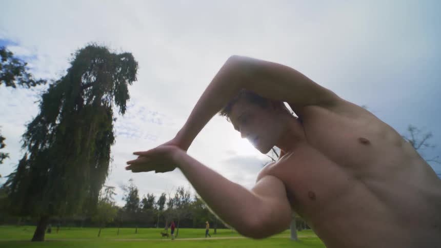 A young white male stretches in a park