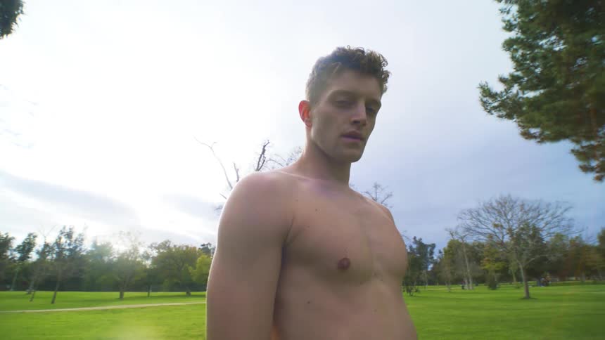 A shirtless man stands outside