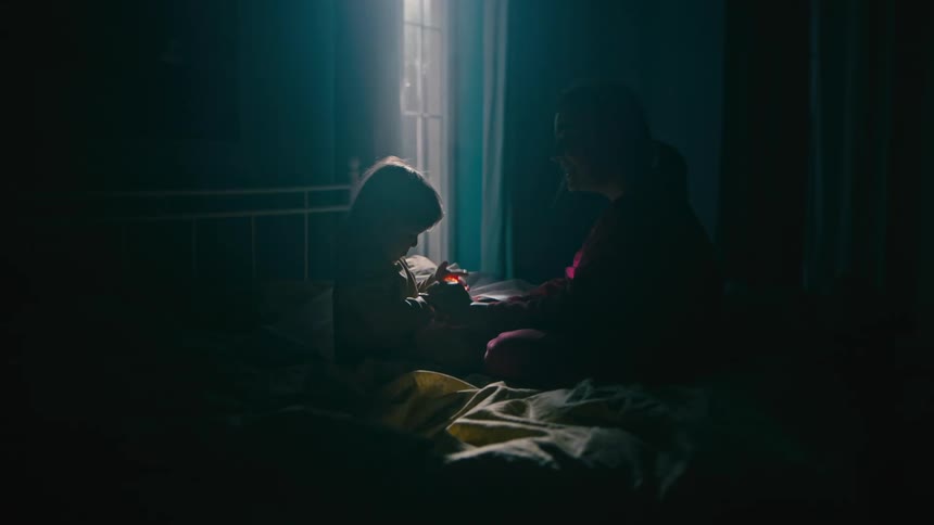 Mother and daughter on a bed waving a flashlight around playfully smiling