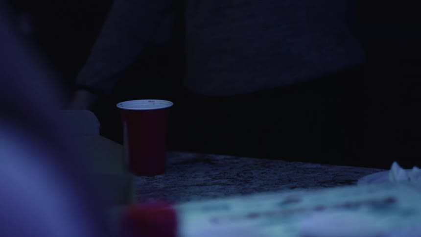 Person standing near a table in the dark picks up a red disposable cup