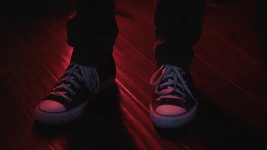 Feet of a person on a laminate floor wearing white and black sneakers