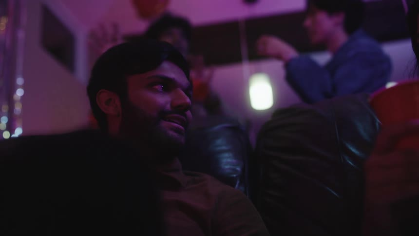 Friends in a purple light environment holding disposable cups of drink talking to each other